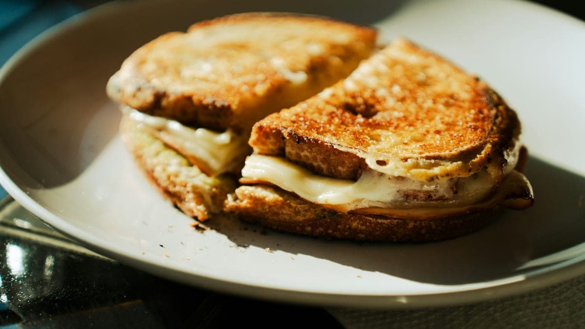 Een krokant gegrilde kaassandwich, doormidden gesneden, met kimchi en gesmolten kaas die tussen het brood vandaan piept.
